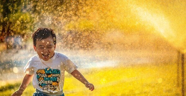 happy kid running through sprinkler