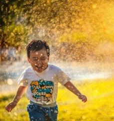 happy kid running through sprinkler