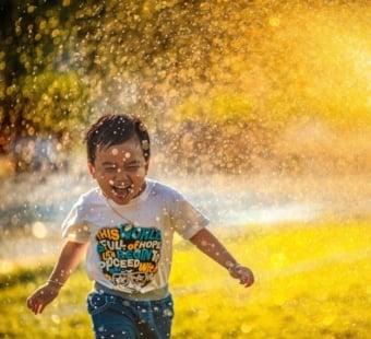 happy kid running through sprinkler
