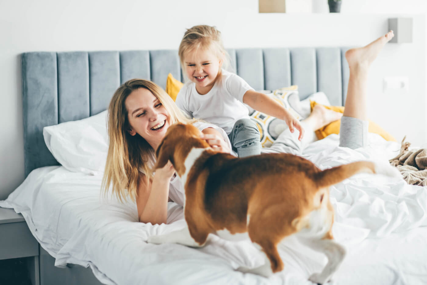 Happy mother and daughter with dog having fun and playing together on the bed at home