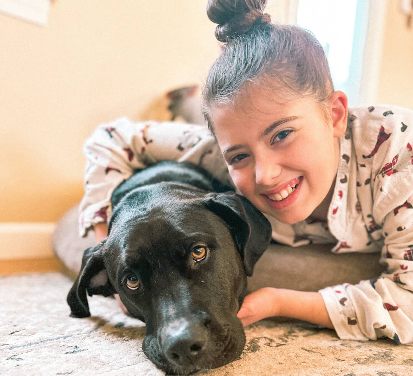 Dani laying on the floor giving her black lab dog a hug