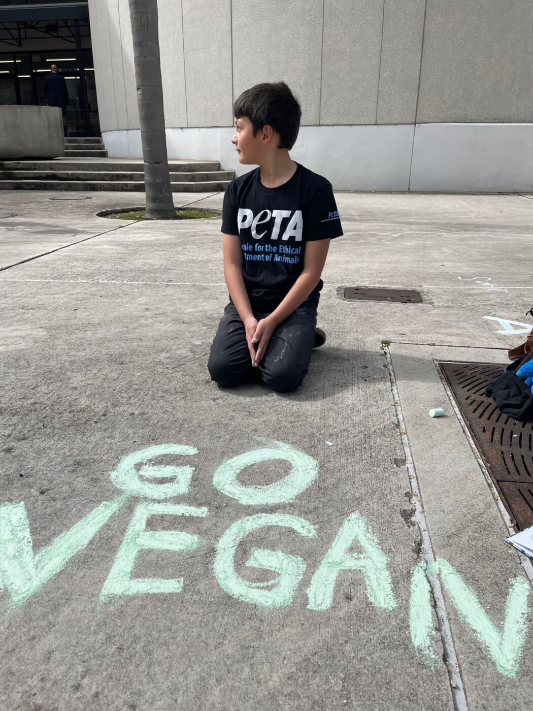 boy in PETA Shirt posing on a driveway in front of chalk art that reads: Go Vegan 