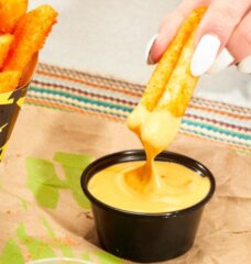 Taco Bell's Nacho Fries being dipped into Vegan Nacho Sauce.