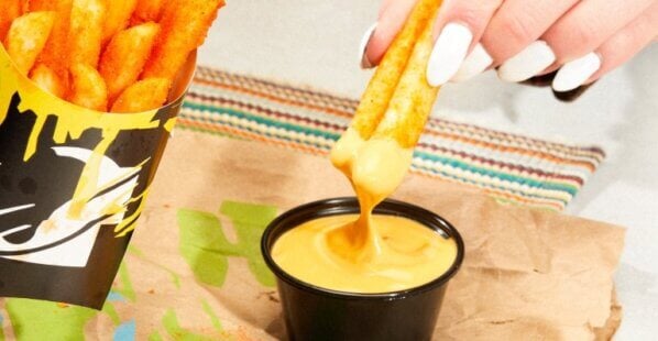 Taco Bell's Nacho Fries being dipped into Vegan Nacho Sauce.