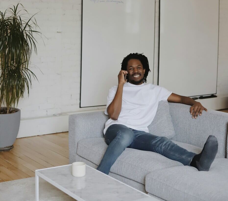 man on the couch on the phone in a white shirt and jeans