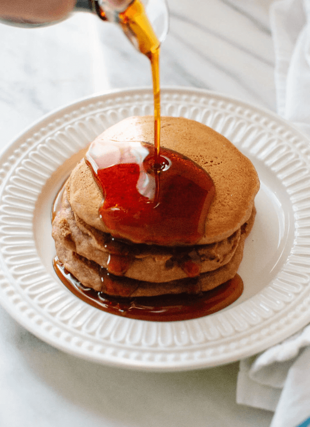 plate of pancakes with maple syrup being poured on them.