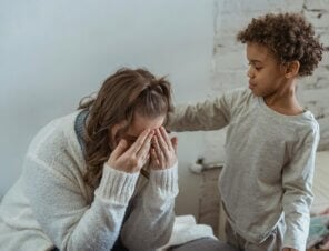 son is comforting his mom by touching her back while she cries.