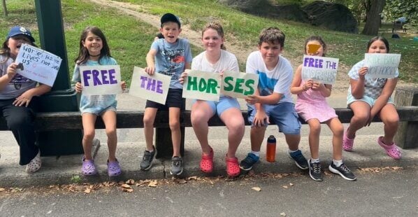 group of kids at central park holding signs to protest aginst horse-drawn carriages