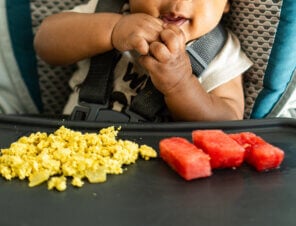 baby in a high chair eating tofu scramble and watermelon