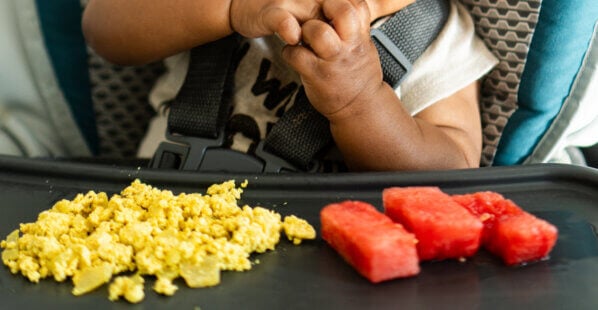 baby in a high chair eating tofu scramble and watermelon